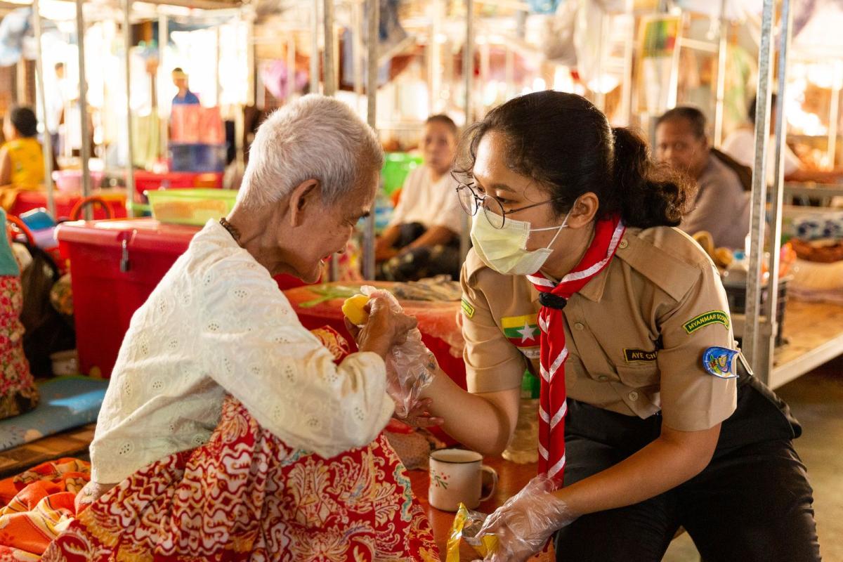 A Scout helps an elderly woman during an outreach programme